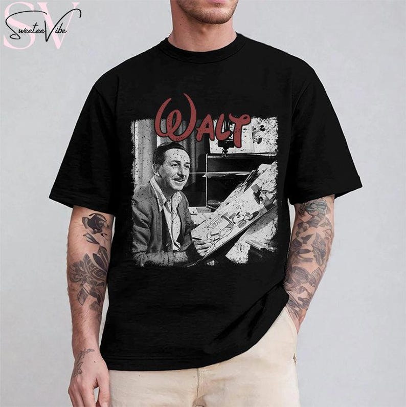 May include: Black t-shirt featuring a vintage-style graphic of Walt Disney, with the name "Walt" in red script. The image shows Walt Disney in a black and white photo, seated and drawing. The shirt is a classic crew neck.