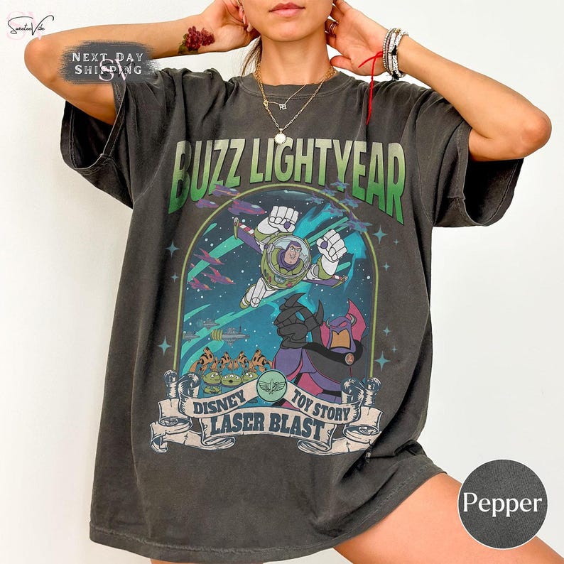 Puede incluir: Camiseta gris oscuro con un dise&ntilde;o de Buzz Lightyear de Toy Story. El dise&ntilde;o incluye el texto "BUZZ LIGHTYEAR" en verde y "DISNEY TOY STORY LASER BLAST" en una pancarta. La camiseta tiene un aspecto vintage y desgastado.
