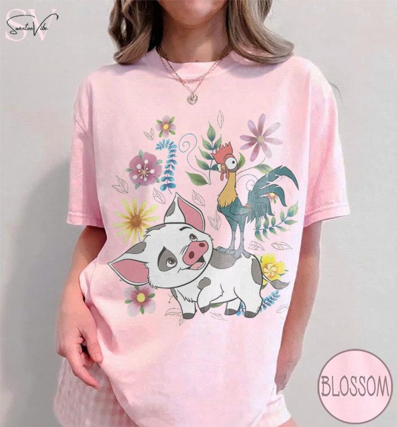 Puede incluir: Camiseta rosa claro con un dise&ntilde;o de cerdo y gallo de dibujos animados, rodeados de flores. El cerdo es blanco con manchas grises y orejas rosas. El gallo es amarillo, verde y azul. La camiseta tiene la palabra "Blossom" en un c&iacute;rculo.