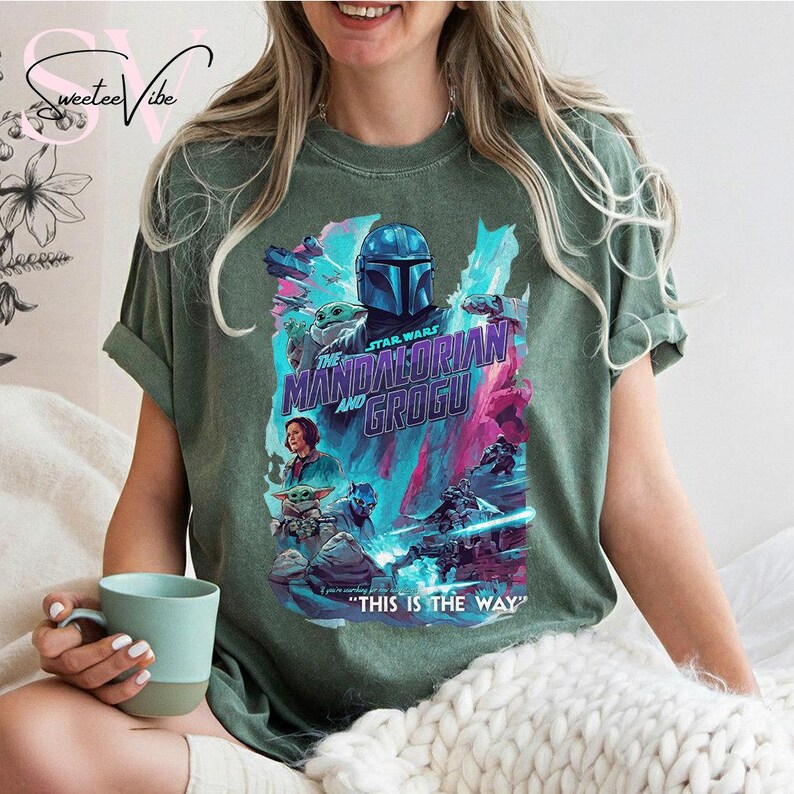 May include: Green t-shirt featuring a colorful graphic from "The Mandalorian" series, with the text "The Mandalorian and Grogu" and "This is the Way". The design includes characters and elements from the show.