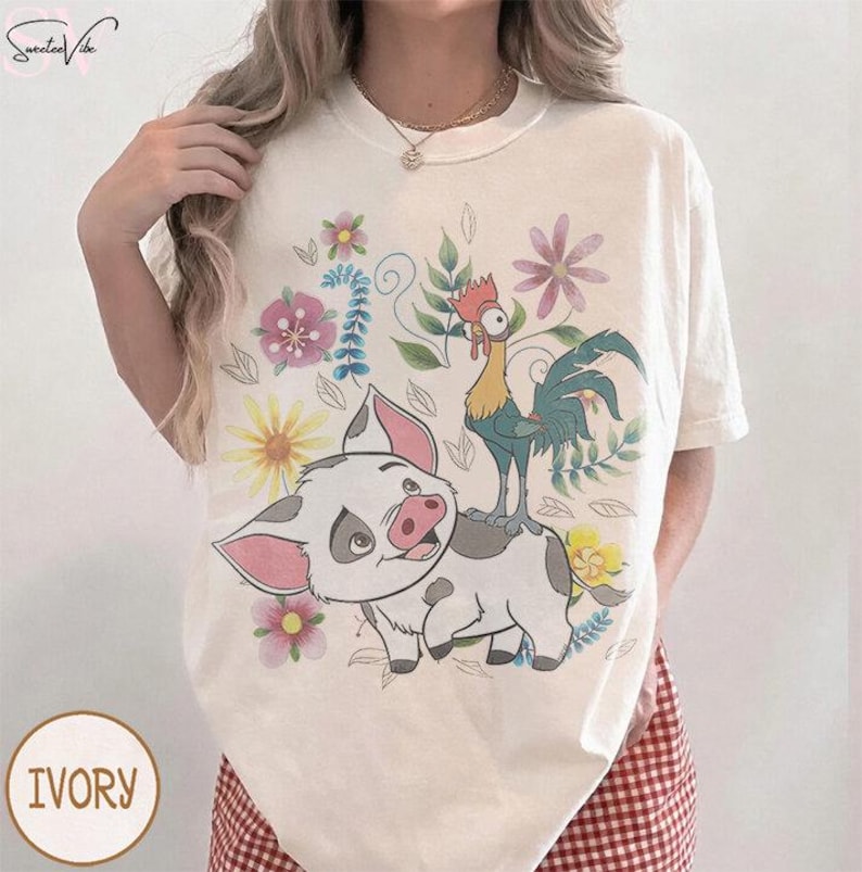 Puede incluir: Camiseta de color marfil con un dise&ntilde;o de cerdo y gallo de dibujos animados, rodeados de flores. El cerdo tiene orejas y hocico rosas. El gallo es amarillo, azul y rojo. La palabra "IVORY" est&aacute; impresa en la camiseta.