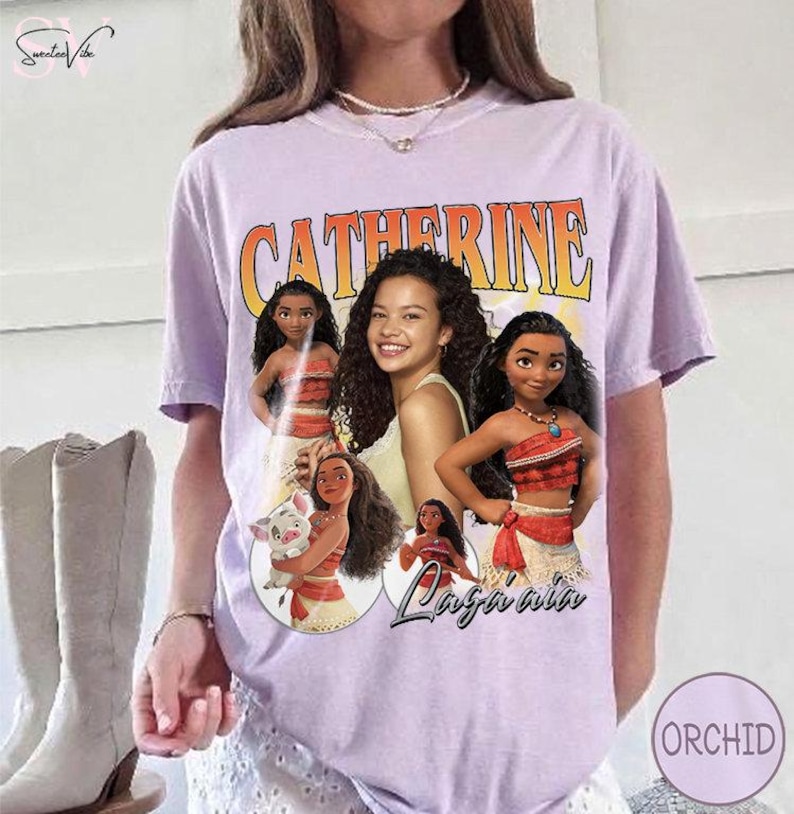 K&ouml;nnte beinhalten: Ein hellviolettes Kurzarm-T-Shirt mit einem Grafikdruck des Namens Catherine in fetten orangefarbenen Buchstaben &uuml;ber einer Collage aus vier animierten Figuren und einem zentralen Portr&auml;t einer Person mit langem, dunklem, lockigem Haar.
