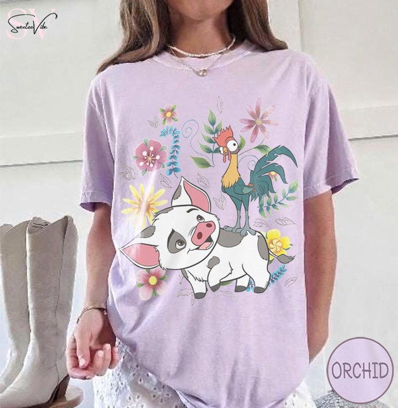 Puede incluir: Camiseta lila claro con un dise&ntilde;o de cerdo y gallo de dibujos animados, rodeado de flores. El cerdo es blanco con manchas grises y orejas rosas, y el gallo es verde, amarillo y rojo. La palabra "ORCHID" est&aacute; en un c&iacute;rculo en la parte inferior derecha.