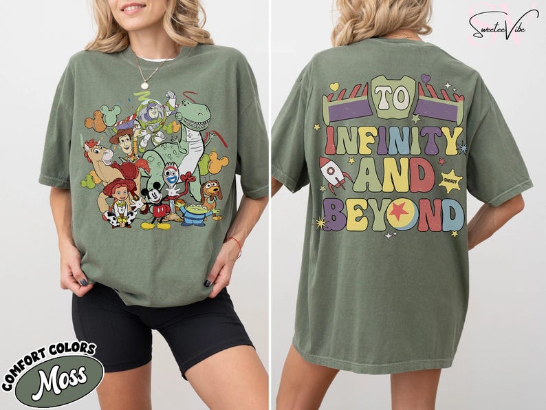 Op de afbeelding: Olijfgroen T-shirt met een kleurrijke afbeelding van Toy Story-personages op de voorkant. De achterkant van het shirt toont de zin "To Infinity and Beyond" in een retro lettertype. Het shirt is een comfort kleur.