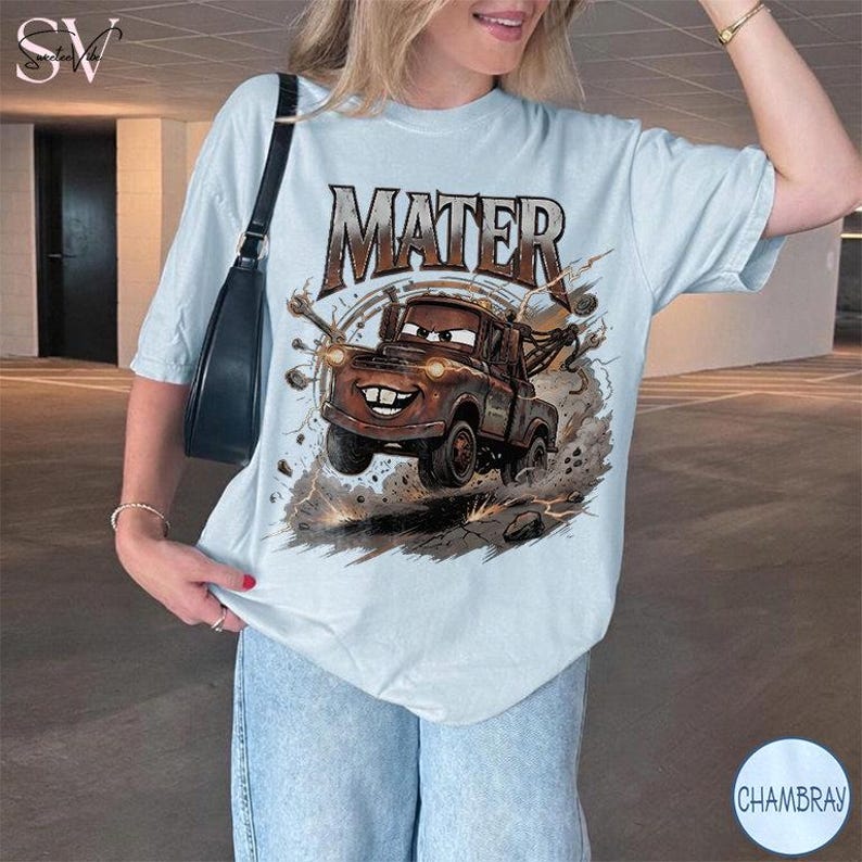 May include: Light blue t-shirt featuring a graphic of Mater from the movie Cars. The brown tow truck is depicted in motion with the word "MATER" above. The shirt is a relaxed fit and has short sleeves.