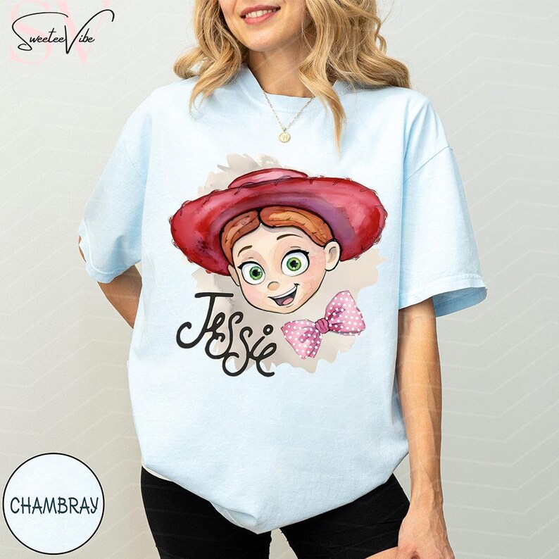 Puede incluir: Camiseta azul claro con una ilustraci&oacute;n de acuarela de Jessie de Toy Story. El dise&ntilde;o incluye la cara de Jessie, un sombrero rojo, un lazo rosa y el nombre "Jessie" en cursiva. Prenda de vestir informal.