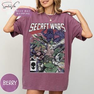 Puede incluir: Camiseta de color bayas con un dise&ntilde;o de portada de c&oacute;mic. Las palabras "SECRET WARS" est&aacute;n en blanco. El gr&aacute;fico muestra personajes de c&oacute;mics. La camiseta tiene un corte holgado y es de material suave.