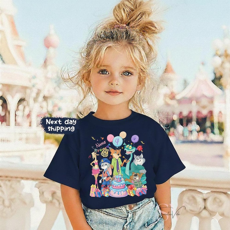 Peut inclure: Un t-shirt bleu marine avec un dessin anim&eacute; color&eacute; de personnages d'animaux, un g&acirc;teau d'anniversaire et des ballons. Le t-shirt porte le texte "Name" au-dessus du dessin et "Next day shipping" dans un encadr&eacute; blanc.