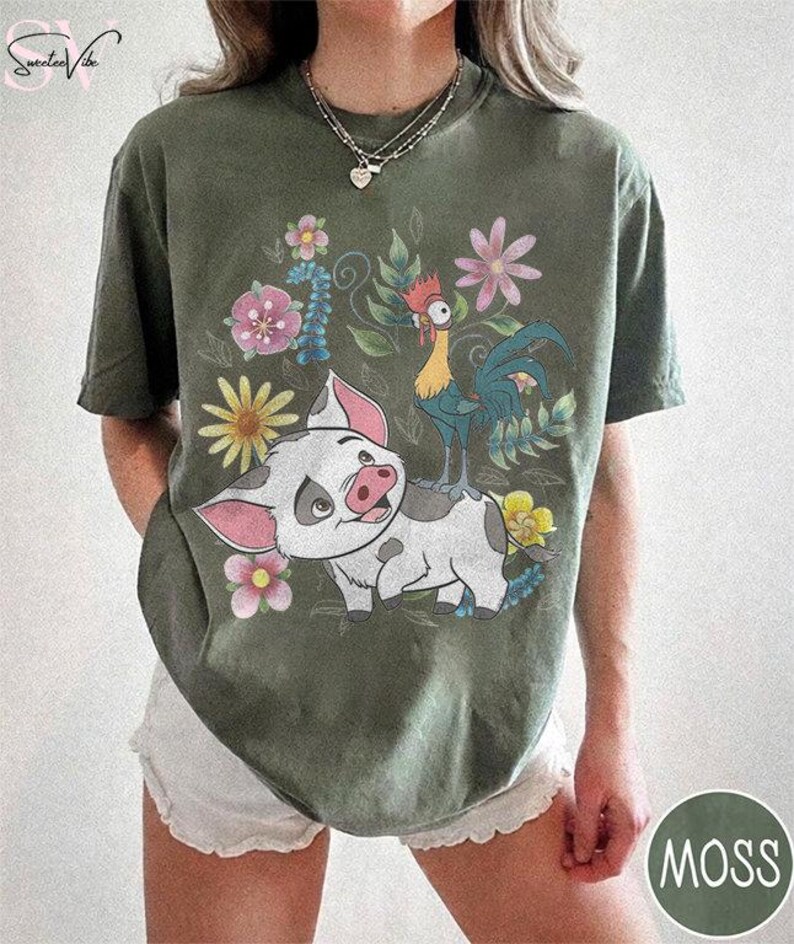 Puede incluir: Camiseta verde musgo con un dise&ntilde;o de cerdo de dibujos animados, gallo y flores. El cerdo es blanco con manchas grises y orejas rosas. El gallo es amarillo y azul. Las flores son rosas, amarillas y azules. La camiseta tiene cuello redondo y mangas cortas.