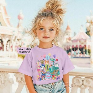 Peut inclure: Un t-shirt lilas avec un dessin anim&eacute; color&eacute; de personnages d'animaux, un g&acirc;teau d'anniversaire et des ballons. Le chiffre 4 est sur un ballon. Les mots "Next day shipping" sont &eacute;galement visibles sur le t-shirt.