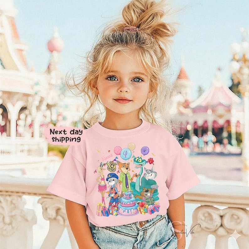 Peut inclure: T-shirt rose avec un motif d'anniversaire de dessin anim&eacute; avec des personnages d'animaux, un g&acirc;teau et des ballons. Le t-shirt porte le texte "Next day shipping" sur le c&ocirc;t&eacute; gauche. Le t-shirt est port&eacute; par une jeune fille.