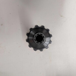 Puede incluir: Una polea de cambio de bicicleta de color gris oscuro con un borde exterior dentado y una abertura central circular. La polea est&aacute; hecha de un material met&aacute;lico y est&aacute; dise&ntilde;ada para su uso en el sistema de transmisi&oacute;n de una bicicleta.