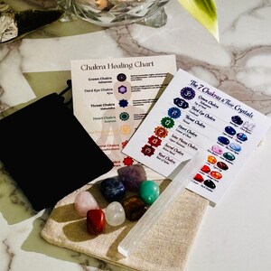 Puede incluir: Un kit de curación de chakras con una bolsa negra con cordón, una bolsa beige y varios cristales de colores. Dos tarjetas muestran información sobre los chakras y asociaciones de cristales. También se incluye una varita de selenita transparente.