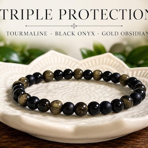 May include: A beaded bracelet featuring alternating round black onyx, gold obsidian, and tourmaline beads. The text TRIPLE PROTECTION TOURMALINE - BLACK ONYX - GOLD OBSIDIAN is displayed above the bracelet, which rests on a white lotus-shaped dish.