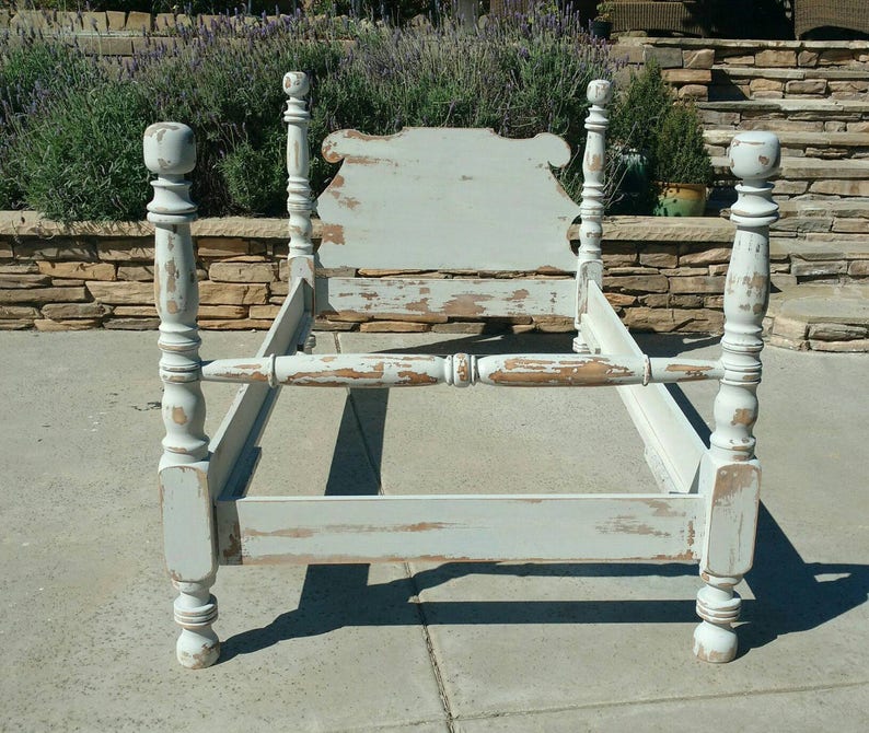 May include: A distressed, light blue bed frame with a headboard and four posts. The frame has a vintage, weathered appearance with visible paint chipping, revealing the wood underneath. The bed frame is designed for a standard mattress size.