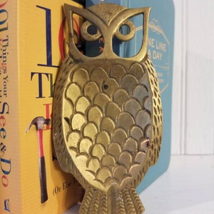 May include: A gold metal owl bookend with a detailed design. The owl has a textured body and large, round eyes.