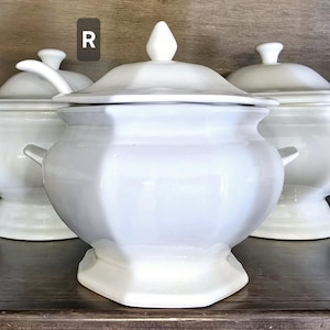 May include: Three white ceramic serving bowls with lids. The center bowl is larger than the other two and has a unique octagonal shape. The bowls are all white and have a glossy finish.
