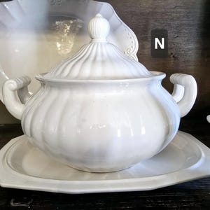 May include: White ceramic serving dish with a lid. The dish has a fluted design and a round shape. The lid has a knob on top.