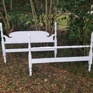 May include: White wooden bed frame with a headboard and footboard. The frame is in a rustic style with turned posts and a simple design.
