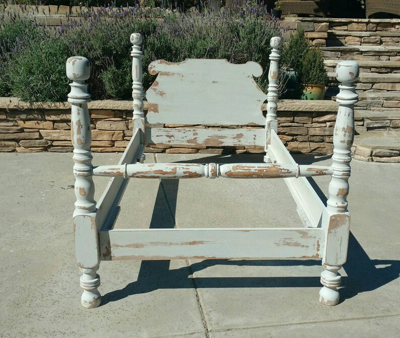 May include: A distressed, light blue bed frame with a headboard and four posts. The frame has a vintage, weathered appearance with visible paint chipping, revealing the wood underneath. The bed frame is designed for a standard mattress size.