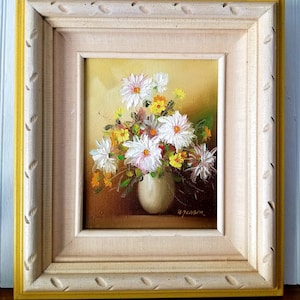 May include: A framed oil painting of a white and yellow flower bouquet in a white vase. The painting is signed "B. Jensen" in the bottom right corner.