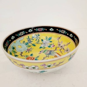May include: A yellow porcelain bowl with a black rim and floral and bird design. The bowl has a white interior and a yellow exterior with a black rim. The design features a bird perched on a branch with flowers and leaves.