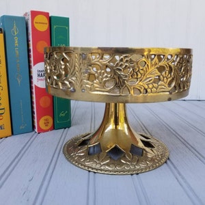 May include: Gold metal decorative stand with a round top and three legs. The top of the stand has a decorative, openwork design with floral motifs.