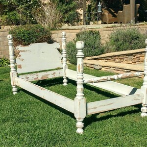 May include: A distressed, light blue bed frame with four tall, turned posts. The headboard has a decorative shape, and the paint is chipped, revealing the wood underneath. The bed frame is set on a green lawn.
