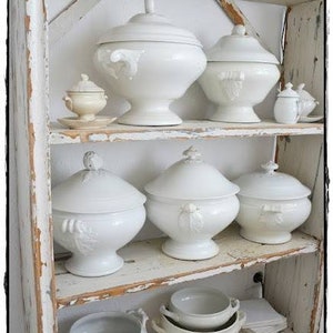 May include: A white wooden shelf unit with multiple white porcelain serving dishes and bowls. The shelf unit has a distressed white paint finish.