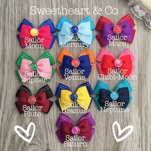 May include: Ten colorful hair bows with different colored ribbons and jeweled centers. Each bow is labeled with the name of a Sailor Scout character from the anime series Sailor Moon. The text "Sweetheart & Co" is at the top of the image.