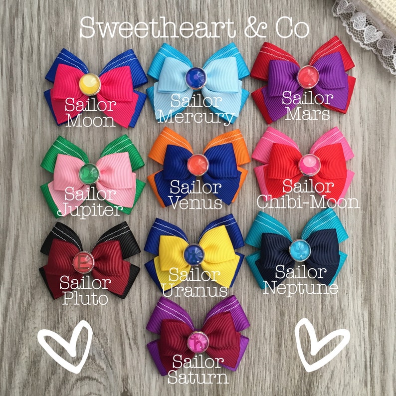 May include: Ten colorful hair bows with different colored ribbons and jeweled centers. Each bow is labeled with the name of a Sailor Scout character from the anime series Sailor Moon. The text "Sweetheart & Co" is at the top of the image.