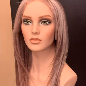 Peut inclure: Tête de mannequin avec une longue perruque à mèches brunes et blondes. Le mannequin est entièrement maquillé, avec fard à paupières, eye-liner et rouge à lèvres. La perruque semble être un modèle frontal en dentelle.