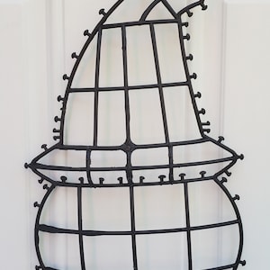 May include: Black metal wire frame in the shape of a witch's hat and cauldron. The frame is decorated with small metal tacks.