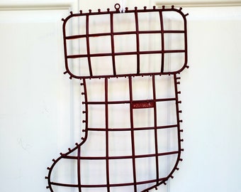 May include: A red wire stocking frame for Christmas decorations. The frame is made of wire and has a rectangular shape with a rounded toe. The frame is hanging from a white string.