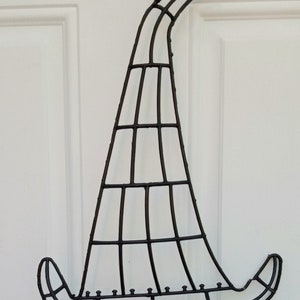 May include: Black metal witch hat decoration. The hat is made of a grid of metal bars, with a curved brim and pointed top. A black ribbon is attached for hanging. Perfect for Halloween.