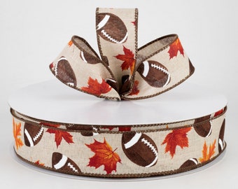 May include: A decorative ribbon featuring a repeating pattern of brown footballs and red, orange, and yellow maple leaves on a beige background. The ribbon is displayed in a bow shape, perfect for fall and football-themed crafts.