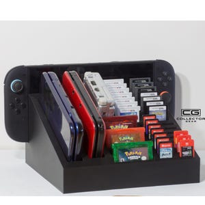 May include: Black wooden gaming console organiser with slots for game cartridges, handheld consoles, and a Nintendo Switch. The organiser holds various game cartridges and handheld consoles. The logo "CG COLLECTOR GEAR" is visible.
