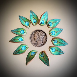 May include: A collection of 10 green and blue peacock feather-shaped polymer clay beads arranged in a circle around a silver coin. The coin is a 1943 Mercury dime with the inscription "IN GOD WE TRUST".