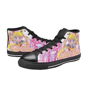 Pu&ograve; includere: Sneakers alte in tela con un design di Sailor Moon. Le scarpe hanno una punta nera, lacci neri e una suola nera. Il design include uno sfondo rosa con personaggi di Sailor Moon e le parole "Sailor Moon".