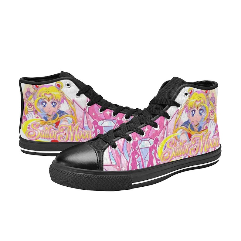Pu&ograve; includere: Sneakers alte in tela con un design di Sailor Moon. Le scarpe hanno una punta nera, lacci neri e una suola nera. Il design include uno sfondo rosa con personaggi di Sailor Moon e le parole "Sailor Moon".