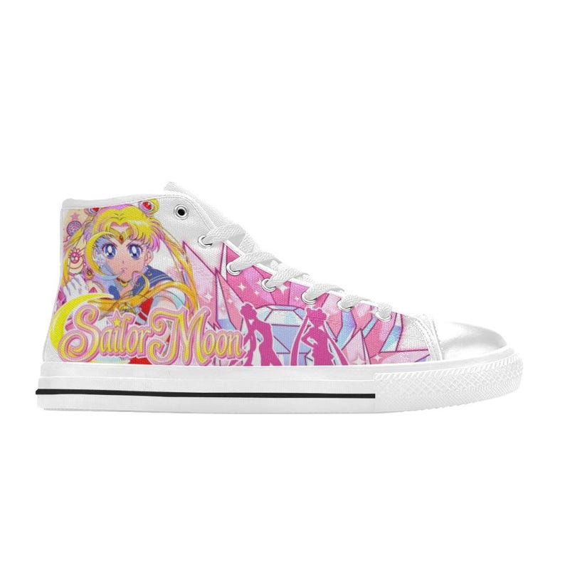 Pu&ograve; includere: Sneaker alta bianca in tela con grafica colorata di Sailor Moon. Il design include il personaggio Sailor Moon, cristalli rosa e la scritta "Sailor Moon" in giallo. La scarpa ha una suola bianca con una striscia nera.
