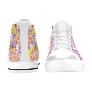 Pu&ograve; includere: Scarpe da ginnastica alte bianche con un colorato design di personaggi anime. Il design include accenti rosa, gialli e blu, con la parola "Sailor" visibile. Le scarpe da ginnastica hanno lacci bianchi e una suola in gomma bianca.