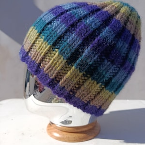 Peut inclure: Un bonnet tricoté à côtes, orné de rayures violettes, turquoise et vert olive. Le bonnet est fabriqué à partir d'un fil texturé. Ce chapeau fait main est parfait pour l'hiver.