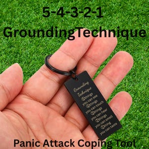 May include: A black rectangular metal keyring engraved with the text: Grounding Technique, 5 things you can see, 4 things you can touch, 3 things you can hear, 2 things you can smell, 1 thing you can taste. The keyring features a black metal ring.