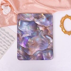 May include: A rectangular tablet case featuring a glossy, iridescent surface with a swirling, multi-tonal pattern of purple, blue, and silver hues that mimic the appearance of polished mother-of-pearl or abalone shell with a smooth finish.