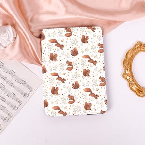 May include: A white rectangular case featuring a repeating pattern of brown squirrels, green sprigs, and yellow dots. The squirrels are in various poses. The case is likely for an electronic device.