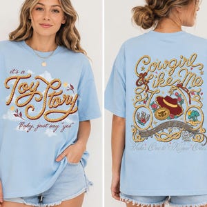 Op de afbeelding: Een lichtblauw t-shirt met een afbeelding op de voorkant met touwachtige tekst "it's a Toy Story, baby, just say 'yes'" en op de achterkant touwranden, een cowboyhoed en de tekst "Cowgirl like Me" en "Takes One to Know One."