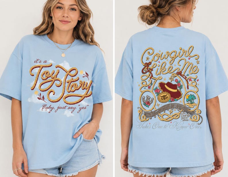 Op de afbeelding: Een lichtblauw t-shirt met een afbeelding op de voorkant met touwachtige tekst "it's a Toy Story, baby, just say 'yes'" en op de achterkant touwranden, een cowboyhoed en de tekst "Cowgirl like Me" en "Takes One to Know One."