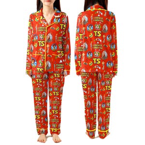 May include: A red long-sleeve pajama set with a button-down top and matching pants. The fabric features a repeating pattern of cartoon characters, colorful balls, and the text "TS" and "I KNEW IT, I KNEW YOU" in yellow and white lettering.