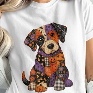 May include: A white short-sleeved t-shirt featuring a graphic of a puppy designed with a patchwork pattern. The dog illustration incorporates various Halloween-themed motifs including orange pumpkins, candy corn, purple flowers, and black spiderwebs.